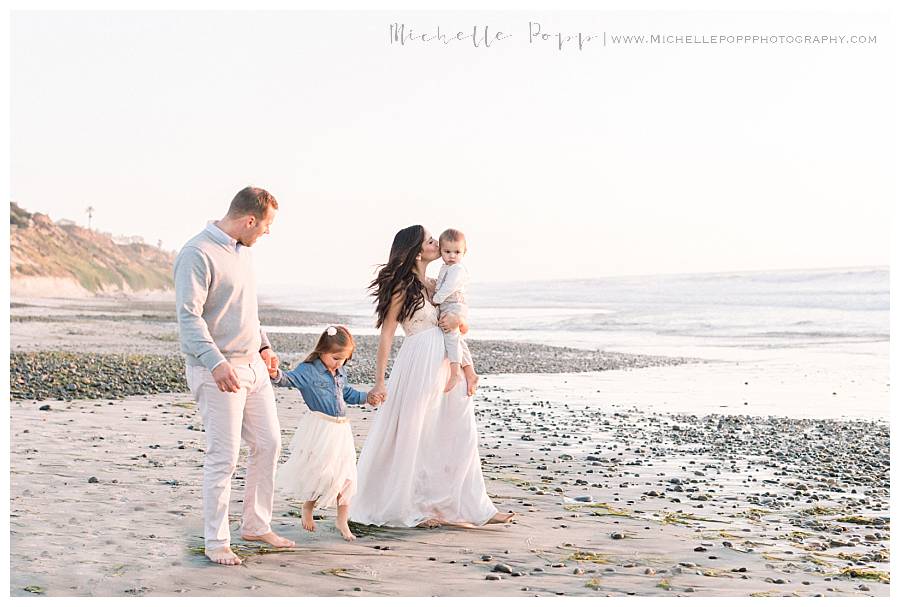 family of four walking along beach holding hands