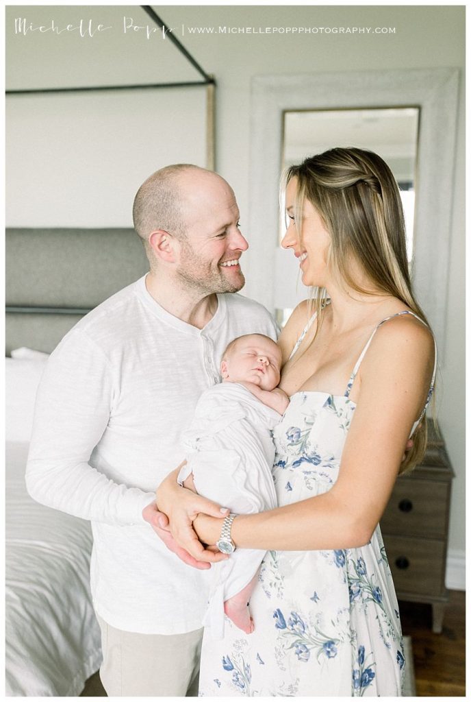 mom and dad smiling at each other while holding baby