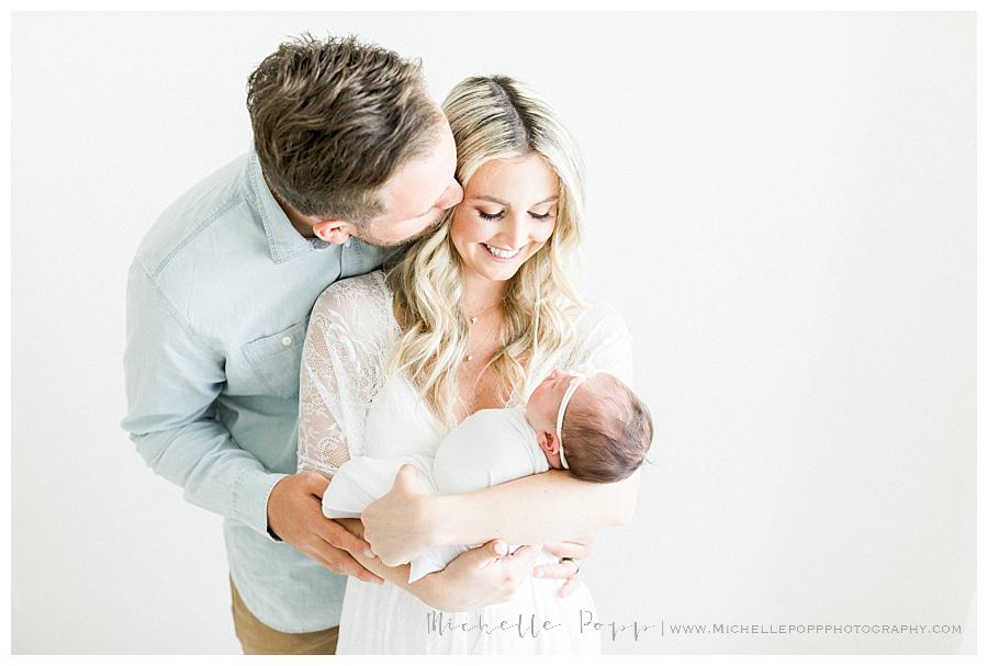 dad kissing mom while she holds baby girl Intimate newborn photography