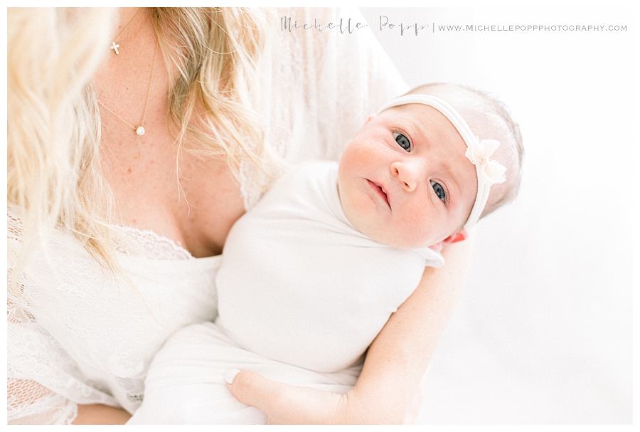 newborn baby in white swaddle looking at camera Intimate newborn photography