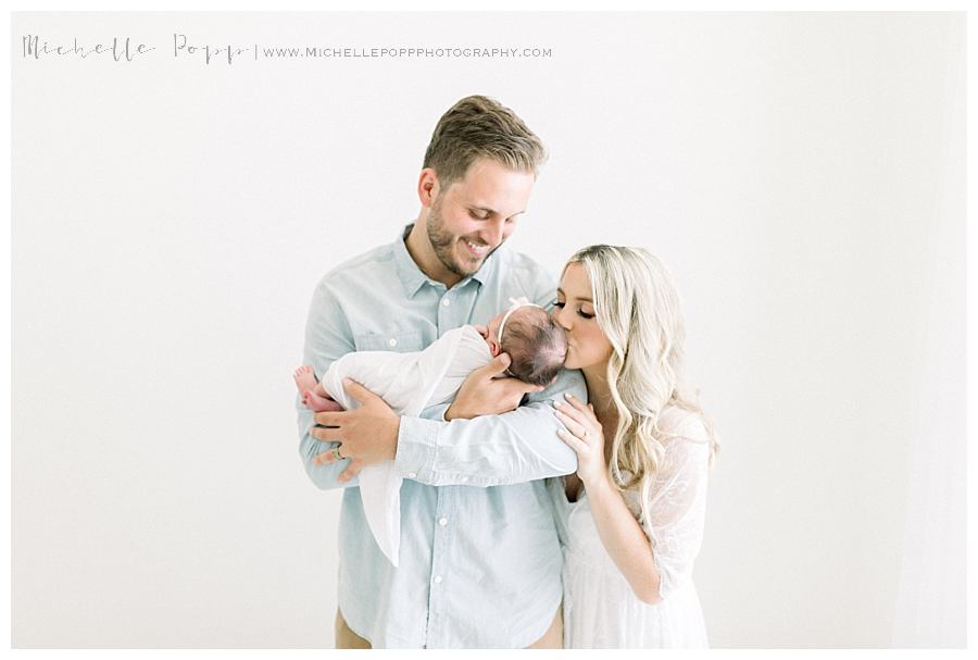 dad holding baby while mom gives kisses Intimate newborn photography