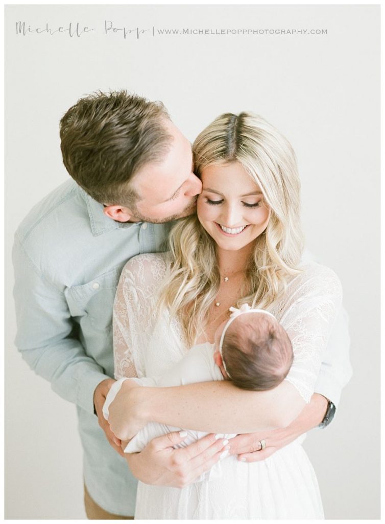 dad giving mom kisses as she holds baby