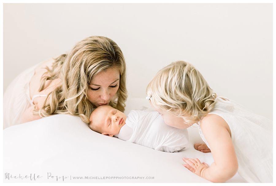 mom and daughter kissing newborn baby boy