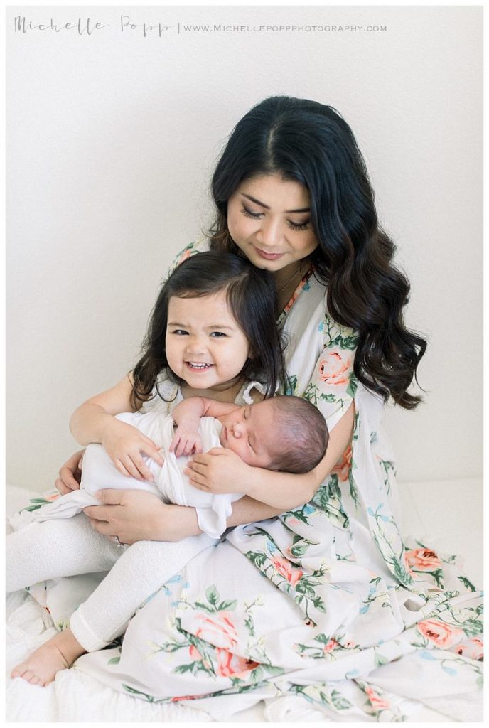 toddler girl smiling as she holds newborn sister