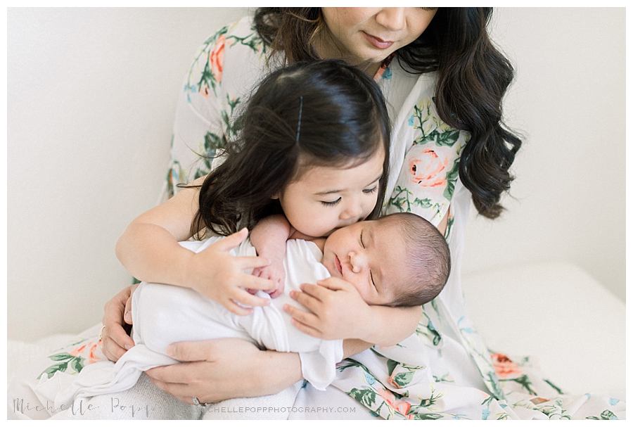 toddler girl giving new baby sister kisses