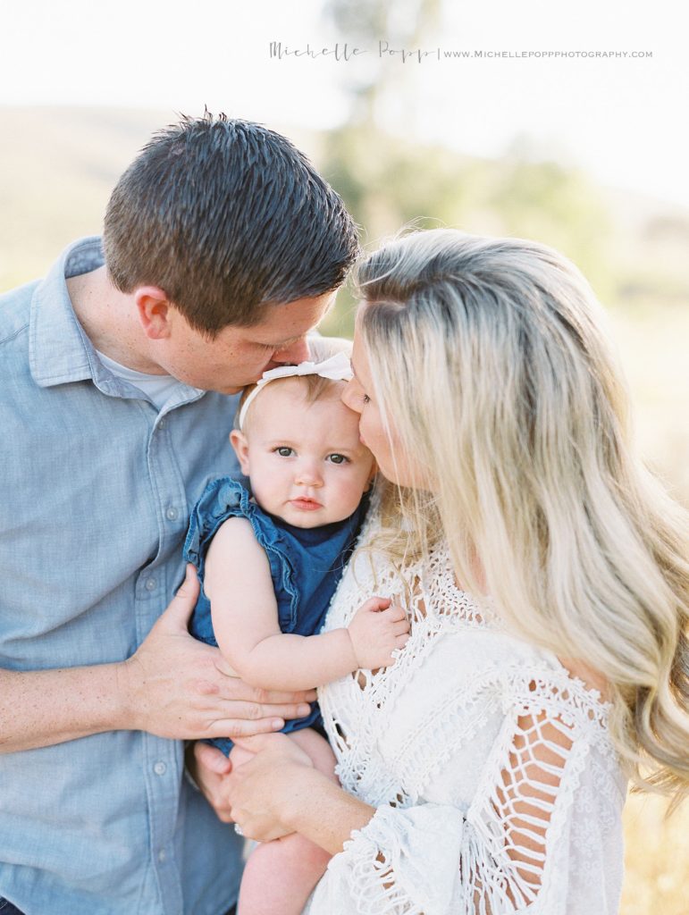 mom and dad kissing baby girl who just turned one years old