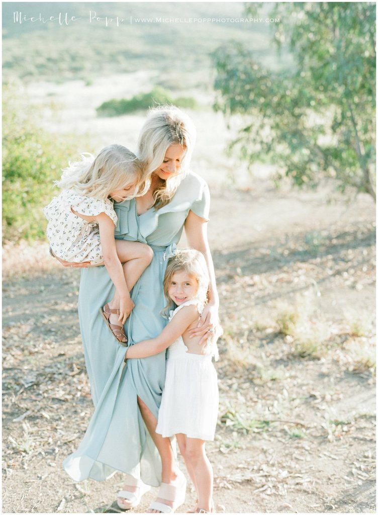 mom holding daughter in one arm and hugging another in other arm