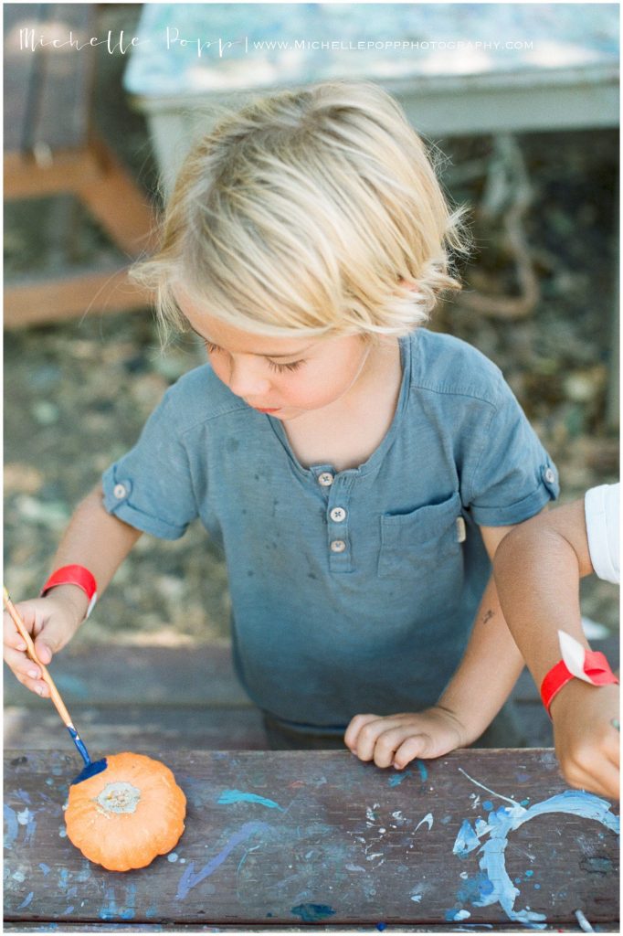 little boy in blue shirt painting pumpkins