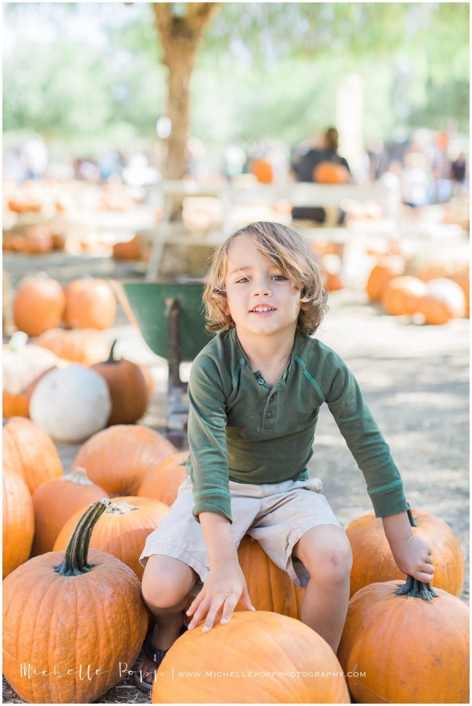 boy in green shirt sitting on a pumpkin