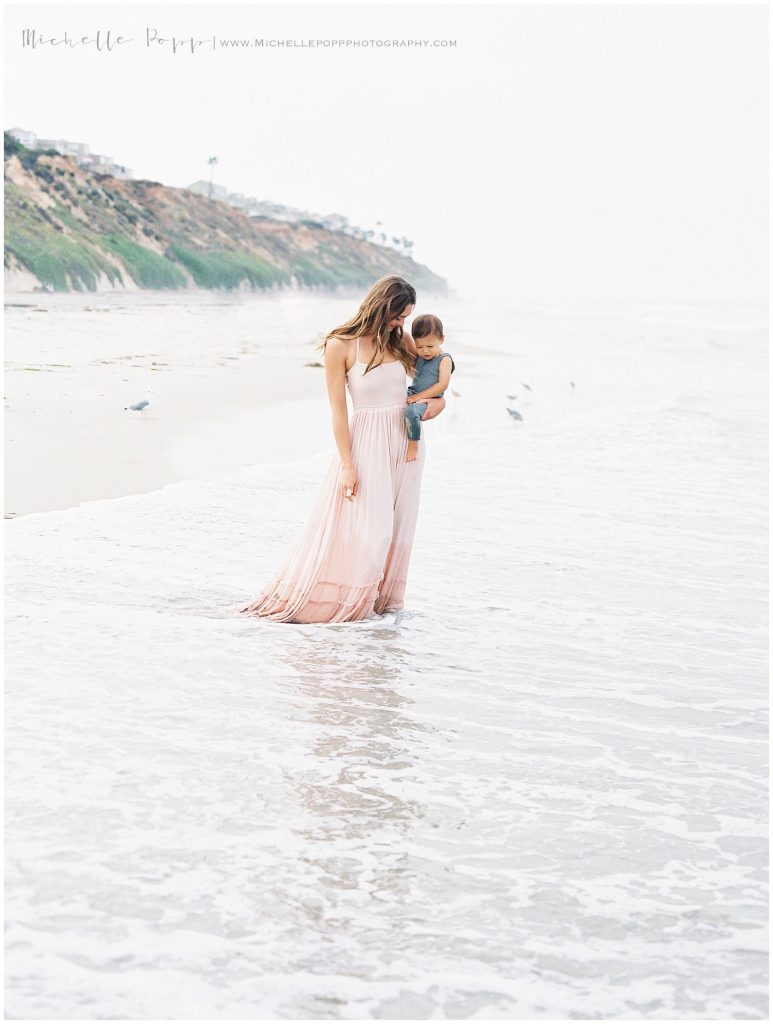 mom holding son while walking in the ocean