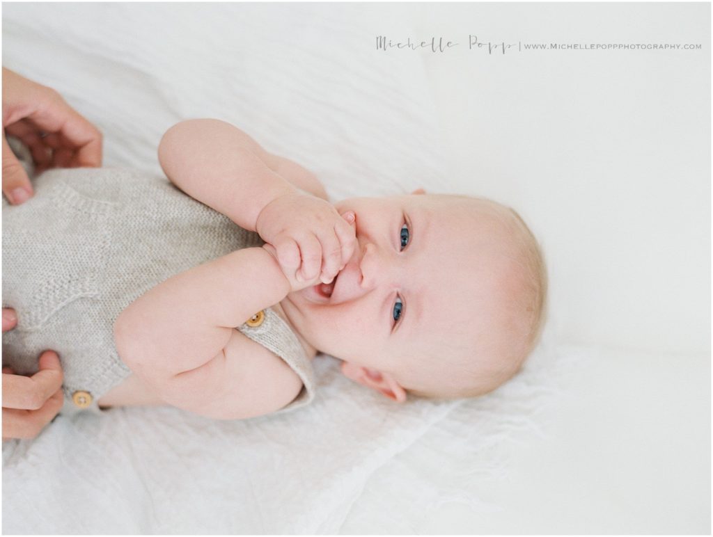 6 month old baby smiling with hands in his mouth 