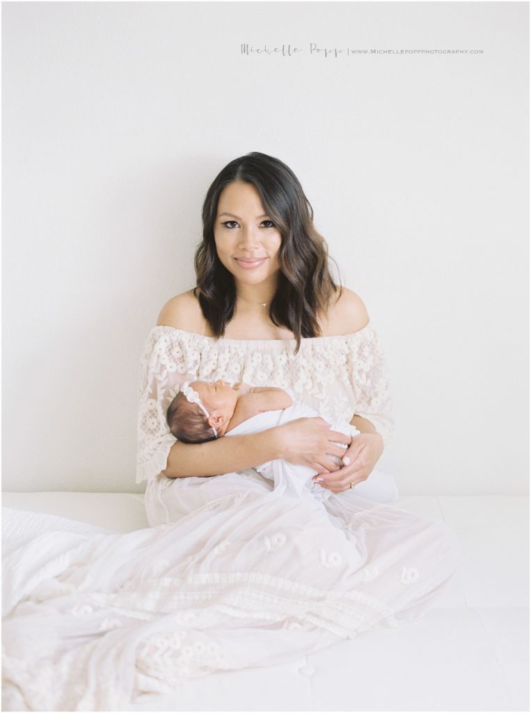 mom smiling at the camera holding baby in newborn photography studio 