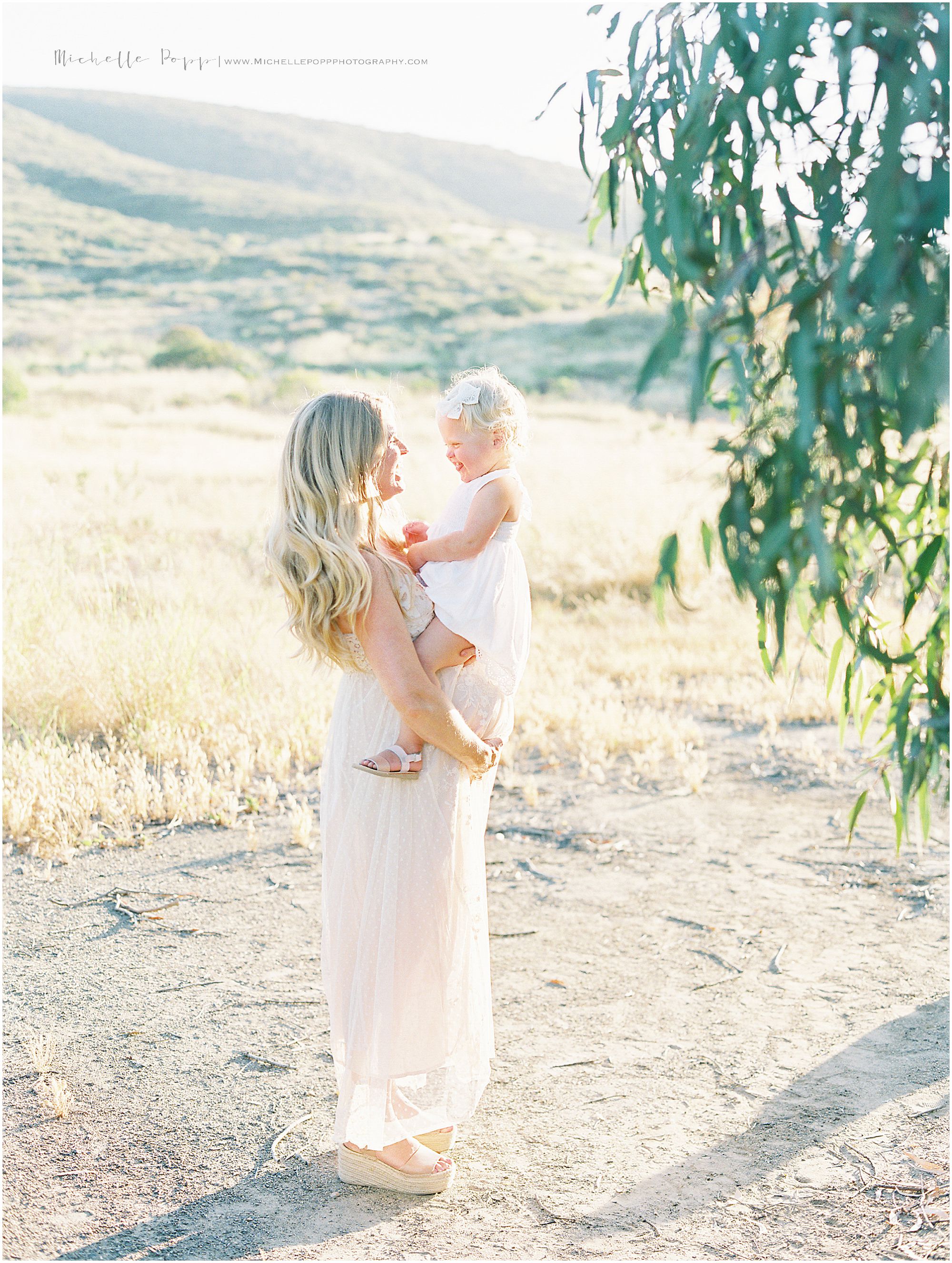 mom holding daughter in field over her baby bump